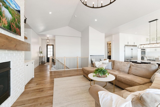 living room featuring vaulted ceiling, recessed lighting, light wood-style flooring, a fireplace, and an inviting chandelier