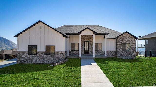 modern farmhouse with stone siding, roof with shingles, board and batten siding, and a front yard