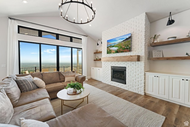 living room with wood finished floors, recessed lighting, vaulted ceiling, a brick fireplace, and a notable chandelier