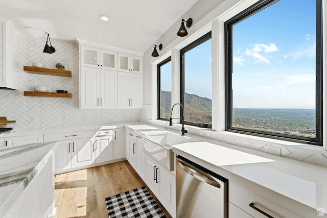 kitchen featuring open shelves, decorative backsplash, light wood-style flooring, stainless steel dishwasher, and a sink