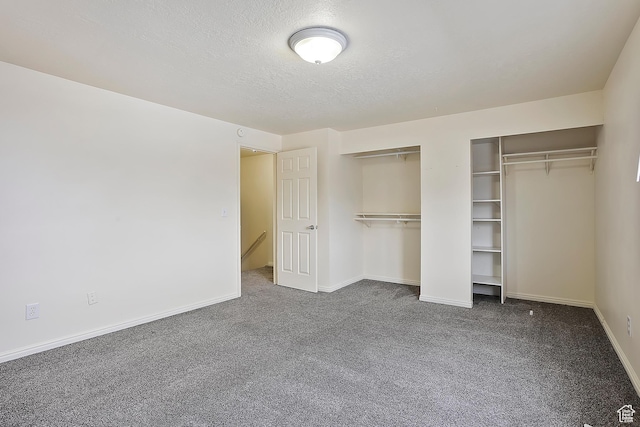 unfurnished bedroom featuring a textured ceiling, two closets, baseboards, and dark colored carpet