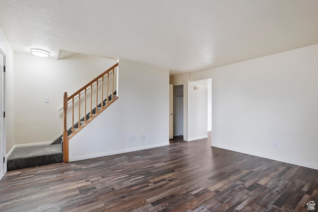 unfurnished living room featuring stairway, baseboards, dark wood-style flooring, and a textured ceiling