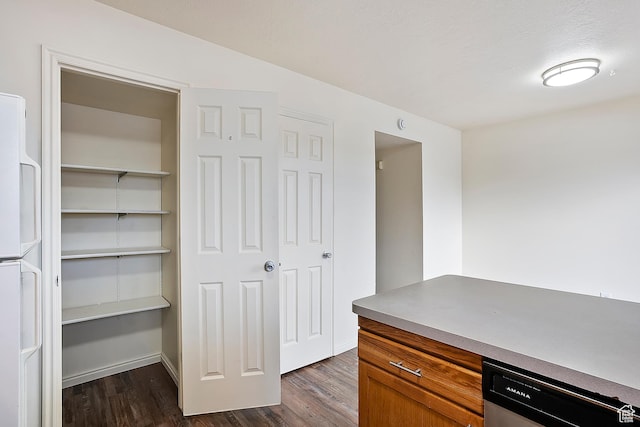 kitchen with brown cabinets, stainless steel dishwasher, dark wood-style flooring, and freestanding refrigerator