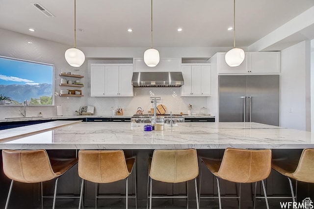kitchen with built in refrigerator, a large island, white cabinets, and wall chimney range hood