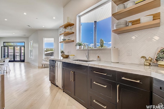 kitchen featuring light stone counters, backsplash, a sink, open shelves, and light wood-style floors