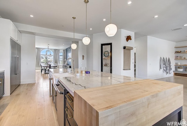 kitchen with stainless steel built in fridge, light wood-style flooring, light stone countertops, and a large island with sink