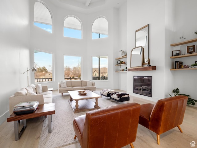 living room featuring a high ceiling, wood finished floors, and a glass covered fireplace