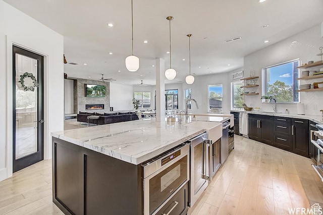 kitchen with light wood finished floors, stainless steel microwave, a ceiling fan, open shelves, and beverage cooler