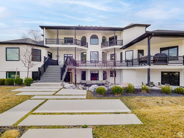 back of house with a balcony, a lawn, stucco siding, and stairway