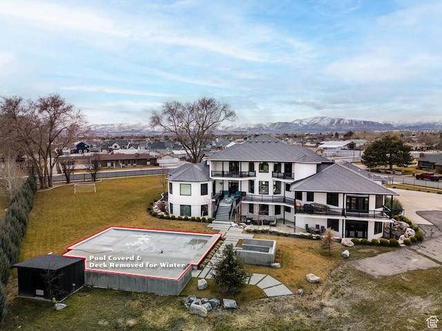 rear view of house featuring roof with shingles, a balcony, a residential view, a lawn, and a mountain view