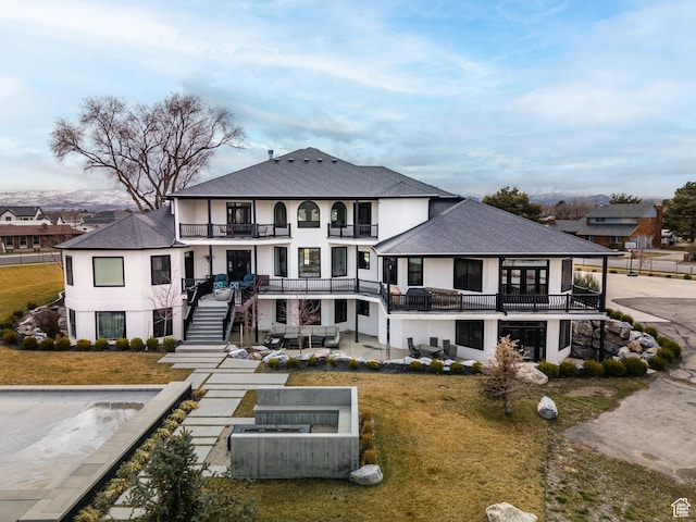 rear view of property featuring a balcony, stairway, stucco siding, a shingled roof, and a patio area