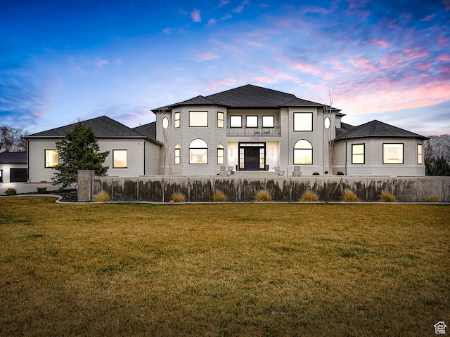back of property at dusk featuring a balcony, a fenced front yard, and a yard