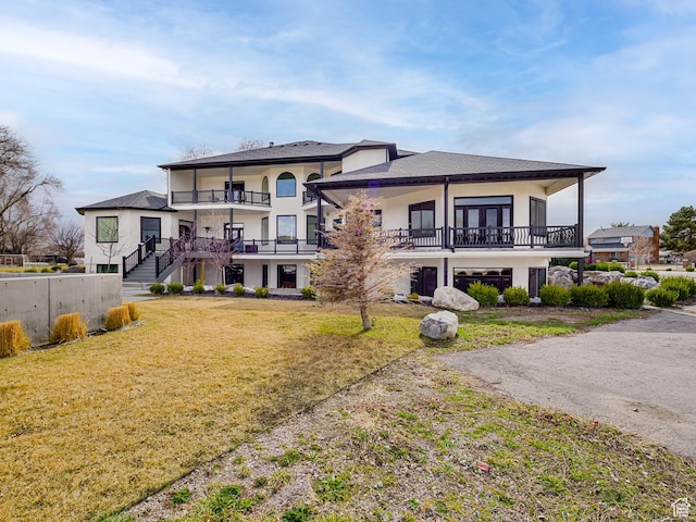 back of house with a balcony, a yard, and stucco siding