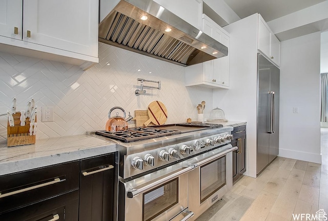 kitchen featuring light stone counters, premium appliances, light wood-style flooring, custom range hood, and white cabinets