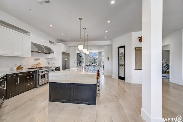 kitchen with white cabinetry, light wood-type flooring, a sink, wall chimney range hood, and premium appliances