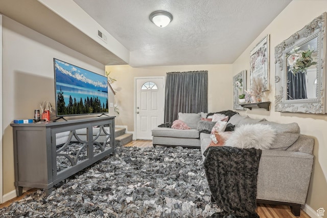 living room featuring visible vents, baseboards, stairs, wood finished floors, and a textured ceiling