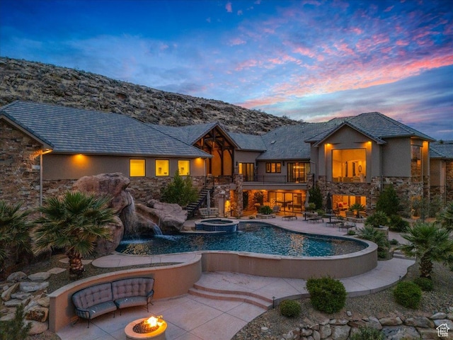 rear view of property featuring stucco siding, stone siding, an outdoor fire pit, stairway, and a patio area