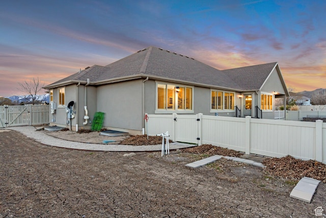 1879 E Tickville Cir, Eagle Mountain, UT 84005 - back of house at dusk featuring a fenced backyard, a gate, roof with shingles, and stucco siding