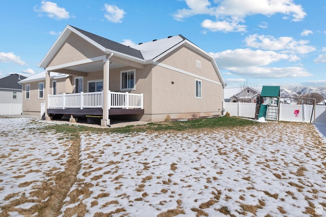 rear view of house featuring stucco siding, a playground, and fence