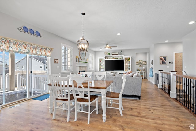 dining room with a fireplace, light wood-style flooring, ceiling fan with notable chandelier, recessed lighting, and visible vents