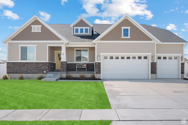 craftsman inspired home with a garage, a front lawn, driveway, and stone siding
