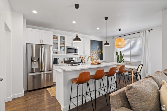 kitchen featuring backsplash, a kitchen breakfast bar, appliances with stainless steel finishes, glass insert cabinets, and dark wood-style floors