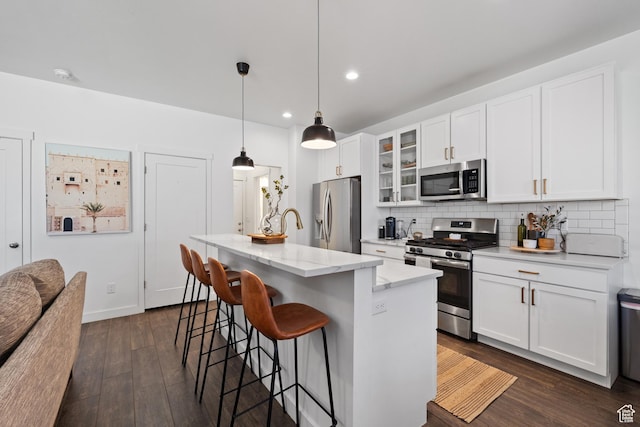 kitchen featuring backsplash, a breakfast bar, appliances with stainless steel finishes, a center island with sink, and dark wood-style flooring