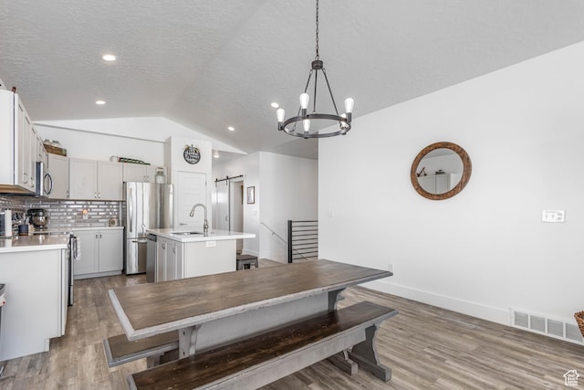 671 W 660 S, Tooele, UT 84074 - dining room featuring wood finished floors, an inviting chandelier, a barn door, visible vents, and lofted ceiling