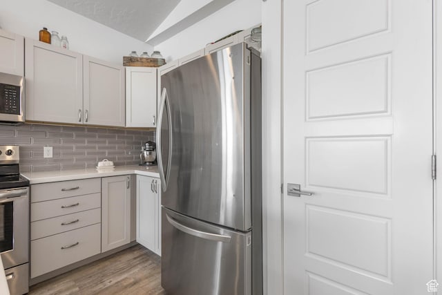 671 W 660 S, Tooele, UT 84074 - kitchen with stainless steel appliances, light countertops, backsplash, vaulted ceiling, and light wood-style flooring
