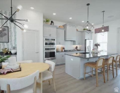 kitchen featuring light wood-style flooring, an island with sink, recessed lighting, stainless steel double oven, and a kitchen bar