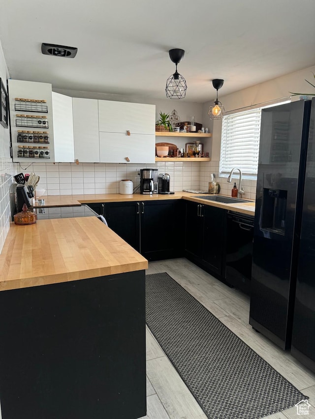 kitchen featuring tasteful backsplash, a sink, butcher block counters, dark cabinetry, and black appliances