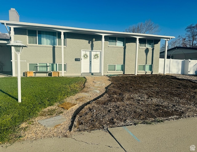 view of front of house with a chimney, fence, a front lawn, and brick siding