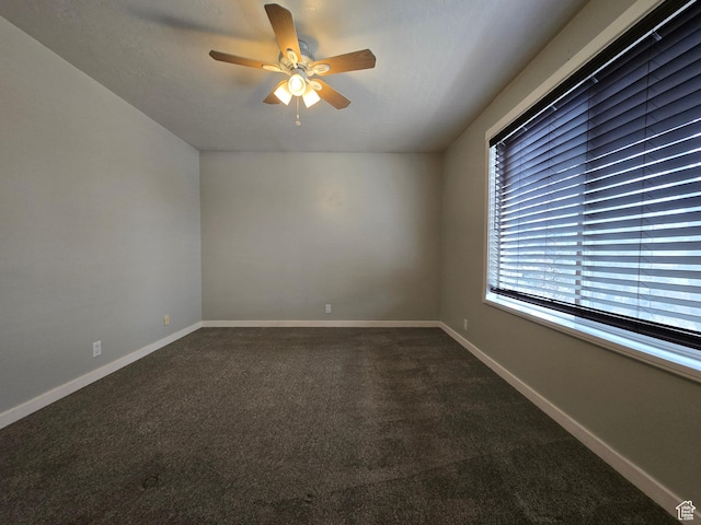 empty room featuring a ceiling fan, dark colored carpet, and baseboards
