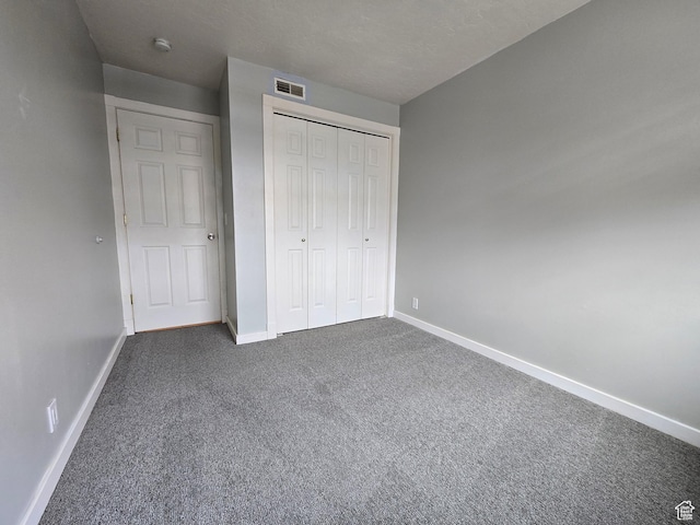 unfurnished bedroom with baseboards, dark colored carpet, and a closet
