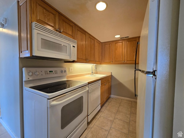 kitchen with white appliances, a sink, brown cabinetry, baseboards, and recessed lighting
