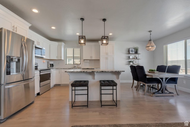 kitchen with backsplash, a center island, a breakfast bar, stainless steel appliances, and white cabinetry