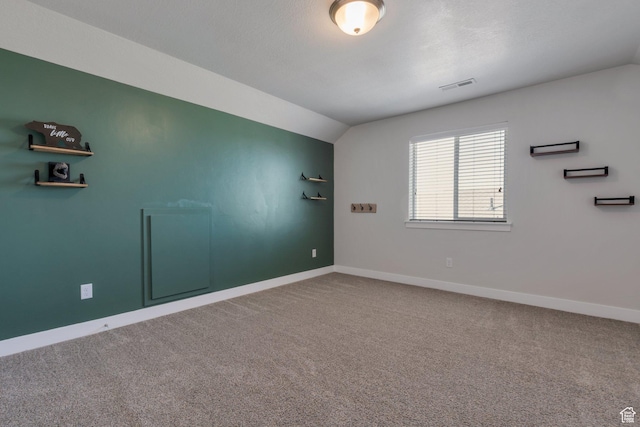 spare room with vaulted ceiling, carpet flooring, baseboards, and visible vents