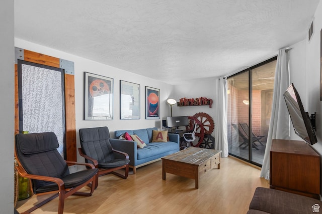 living room featuring expansive windows, a textured ceiling, visible vents, and light wood finished floors