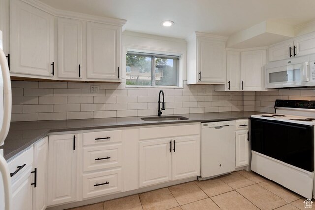 kitchen featuring a sink, dark countertops, white cabinetry, white appliances, and light tile patterned floors
