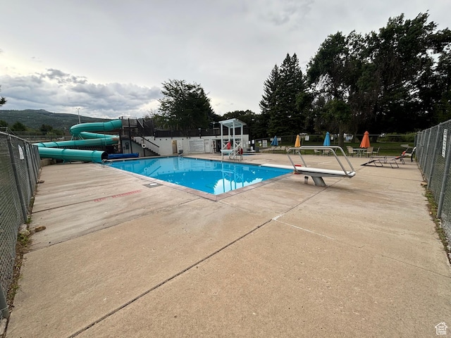 community pool featuring a patio area, a water slide, and fence