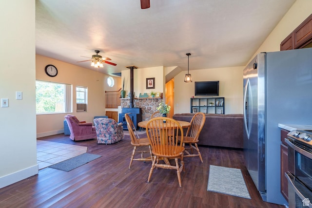 dining space featuring dark wood finished floors, baseboards, a wood stove, and a ceiling fan