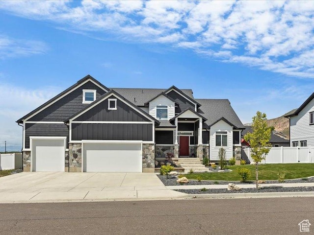 craftsman-style house with a front lawn, driveway, stone siding, fence, and board and batten siding