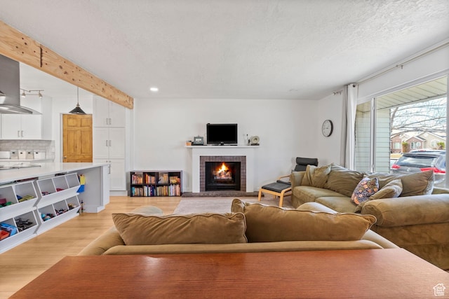 living room with beamed ceiling, a brick fireplace, a textured ceiling, and light wood-type flooring