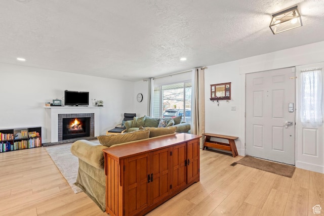 living room with a warm lit fireplace, recessed lighting, light wood finished floors, and a textured ceiling