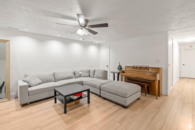 living room featuring light wood finished floors, visible vents, a textured ceiling, and a ceiling fan