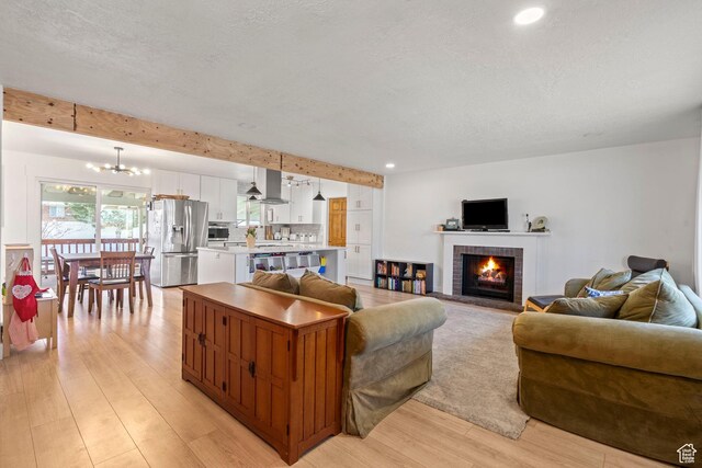 living room featuring light wood-type flooring, a textured ceiling, recessed lighting, a brick fireplace, and a chandelier