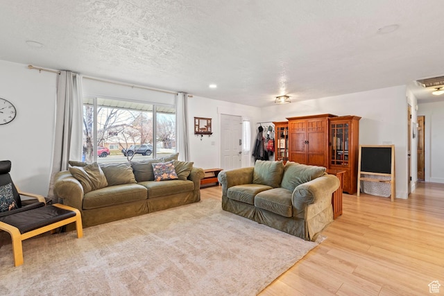 living area featuring visible vents, a textured ceiling, and light wood-style flooring