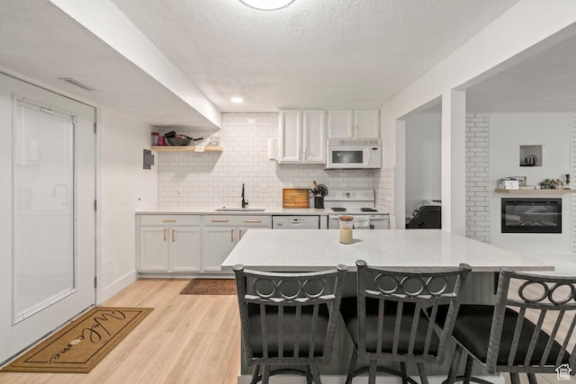 kitchen featuring a sink, a kitchen breakfast bar, white appliances, and white cabinetry