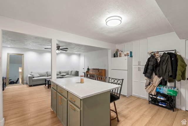 kitchen with a kitchen island, freestanding refrigerator, ceiling fan, a kitchen bar, and light wood-type flooring