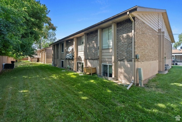 rear view of property featuring brick siding, a lawn, and fence